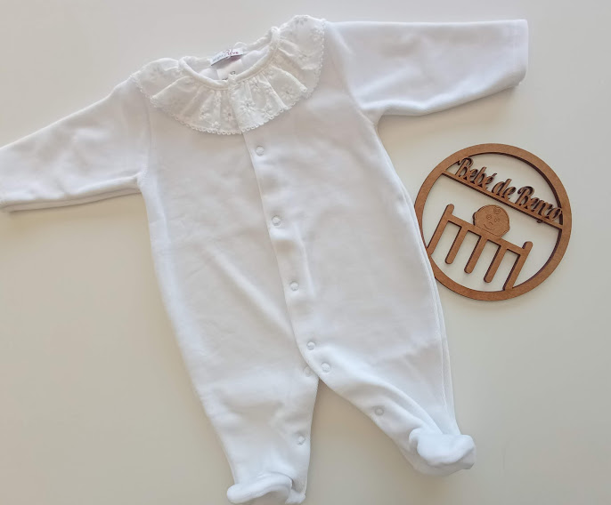 Macacão branco para bebé com gola rendada e botões à frente ao lado de objeto de madeira