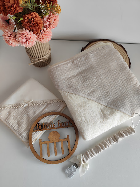 Conjunto de toalha, toalhita, prende-chuchas e placa de madeira 'bebé de berço' com vaso de flores artificiais.