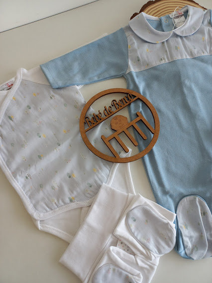 Conjunto de roupa de bebé com body branco com padrões, pijama azul com gola branca, meias brancas e placa de madeira com inscrição