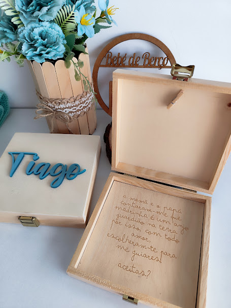 Caixas de madeira com nomes e texto gravado, flores azuis em vaso de madeira e placa redonda decorativa.