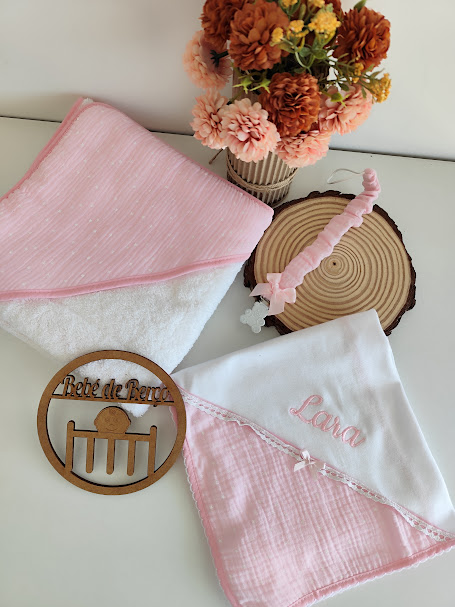 Toalhas de bebé rosa e branco com bordado e acessórios decorativos em superfície branca