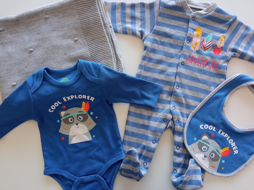 Conjunto de bebé azul com personagem COOL EXPLORER e pijama riscado sobre manta cinzenta