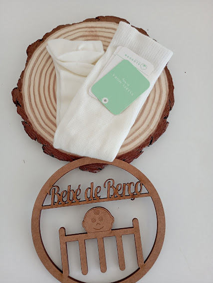 Meias brancas sobre base de madeira com decoração de madeira com texto Bebé de Berço