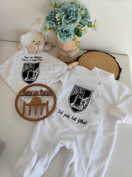 Conjunto de bebé branco com emblema e texto bordado, arranjo floral e ornamento de madeira