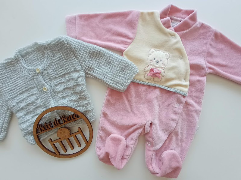 Conjunto de roupa de bebé com malha azul, macacão rosa com bordado de ursinho e placa de madeira com texto