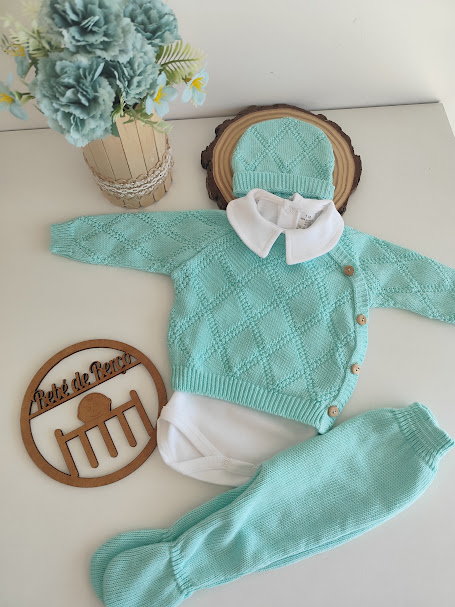 Conjunto de roupa de bebé azul claro e branco exposto em superfície branca com flores e decoração de madeira.