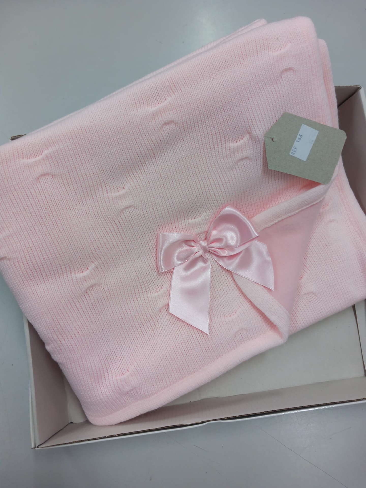 Cobertor rosa claro de malha com padrão em relevo e laço de cetim na caixa