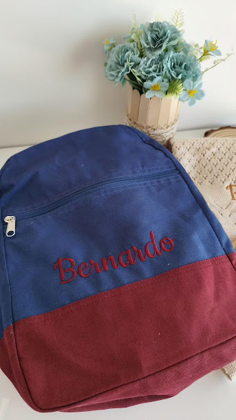 mochila azul e vermelha com nome bordado Bernardo e vaso com flores artificiais