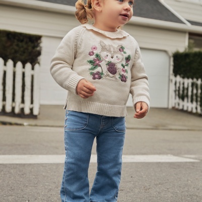 Criança com camisola bege com coelho bordado e calças de ganga azuis