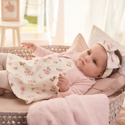 Bebé deitada numa cesta de vime com vestido floral, camisola rosa e faixa de cabelo com laço