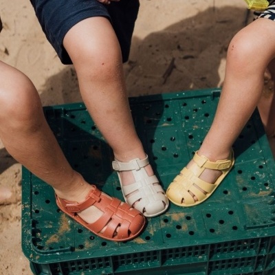 Sandálias infantis coloridas em marrom, branco e amarelo usadas por crianças em caixa verde