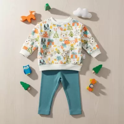 Conjunto de roupa criança com camisola estampada e calças azuis em superfície clara com brinquedos.