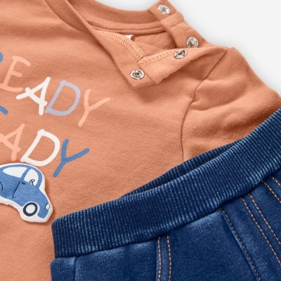 Conjunto de roupa de bebé com t-shirt cor de tijolo e calças azuis.