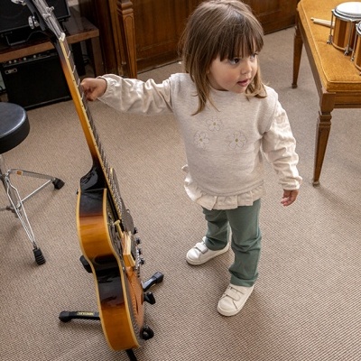 Criança segura guitarra acústica castanha com fundo de piano de madeira