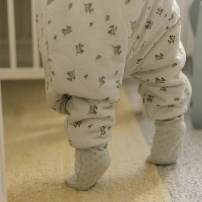 Criança com pijama branco com padrão de flores e meias cinzentas a caminhar sobre tapete amarelo