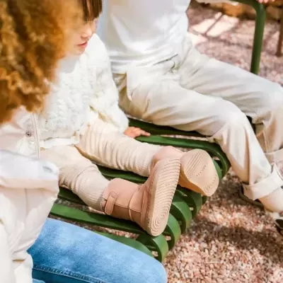 Criança e adultos sentados num banco verde ao ar livre com botas cor de rosa e roupa clara.