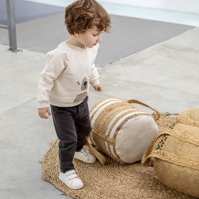 Menino de roupa casual perto de tapete e pufes de fibras naturais.