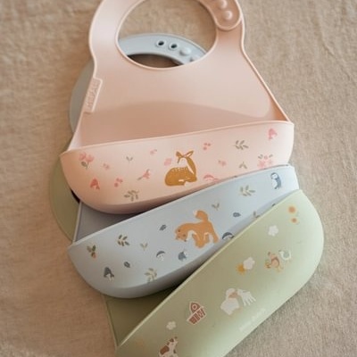 Babetes de silicone coloridos com desenhos infantis e ajuste por botões.