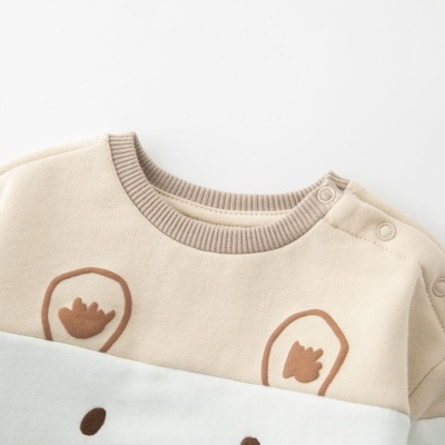 Roupa de bebé bege e branca com estampa de urso e botões no ombro