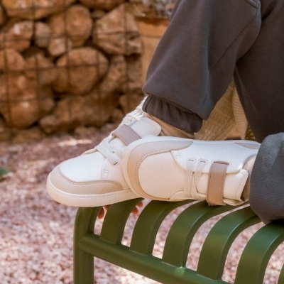 Ténis brancos e bege com fecho velcro sobre banco verde em ambiente exterior de cascalho