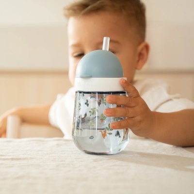 Copo infantil transparente com desenhos e tampa azul com canudo sendo segurado por criança