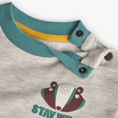 Camisola bege de bebé com decote verde-azulado e estampa de texugo