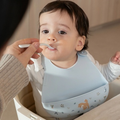 Bebé com babete azul claro com estampas a ser alimentado com colher branca