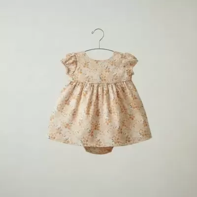 Vestido de bebé com padrão floral em tons de bege, laranja e verde pendurado num cabide.