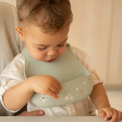 Bebé com babete de silicone verde claro com ilustrações de animais e galinheiro