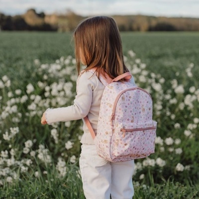 Criança com mochila cor-de-rosa em campo florido