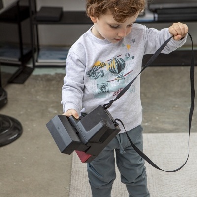 Criança com t-shirt cinzenta e calças azul-acinzentadas a segurar máquina fotográfica preta