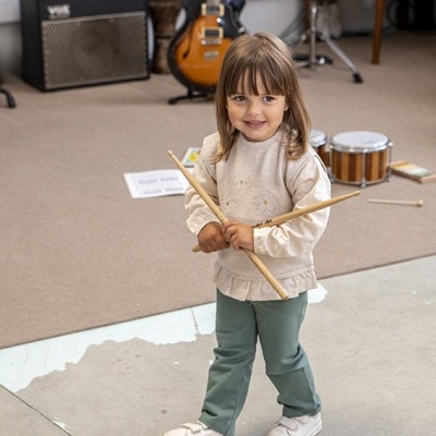 Menina segura baquetas em interiores com instrumentos musicais
