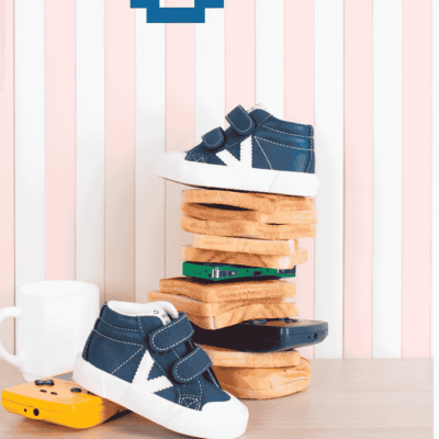 Sapatilhas azul escuro para criança com velcros e detalhes brancos, pão de forma, dispositivo amarelo, caneca branca, fundo riscas rosa e branco