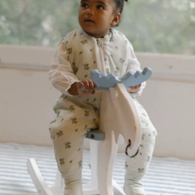 Criança com macacão branco e verde numa balança de madeira branca e azul