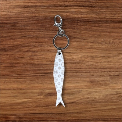 Chaveiro em formato de peixe branco com padrão castanho e fecho metálico sobre madeira