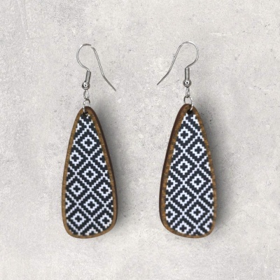 Brincos de madeira com padrão geométrico preto e branco no fundo cinza