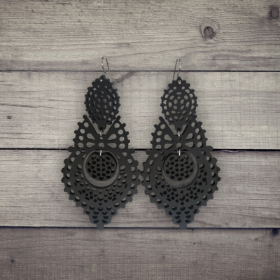 Brincos pretos pendurados com padrão recortado em madeira clara