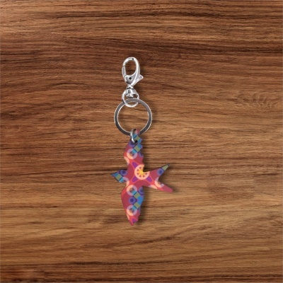 Chaveiro metálico com pendente colorido em forma de pássaro numa superfície de madeira