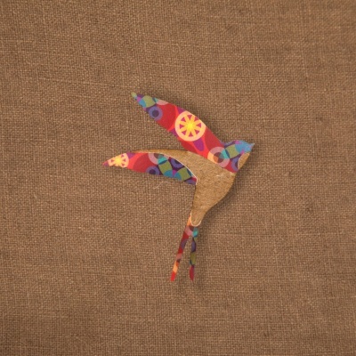 Pássaro decorativo em tecido colorido e madeira sobre fundo têxtil bege