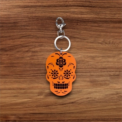 Porta-chaves caveira laranja com padrões pretos sobre fundo de madeira.