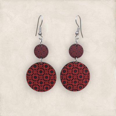 Brincos pendentes em madeira com padrão geométrico preto sobre fundo vermelho e ganchos metálicos prateados