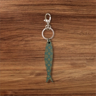 Chaveiro com pingente de peixe azul com padrão dourado sobre fundo de madeira