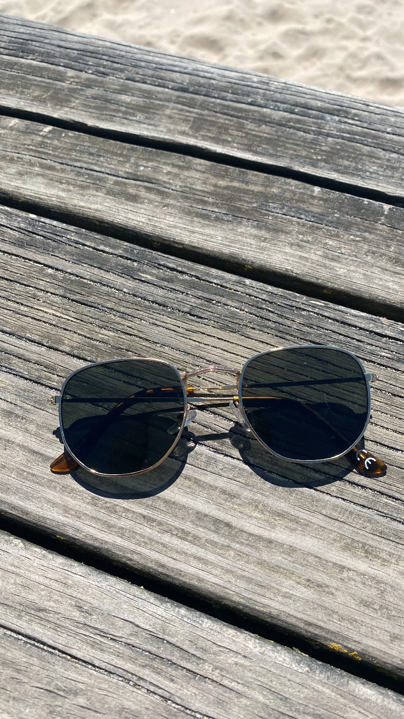 Óculos de sol metálicos com lentes escuras sobre mesa de madeira cinzenta ao ar livre