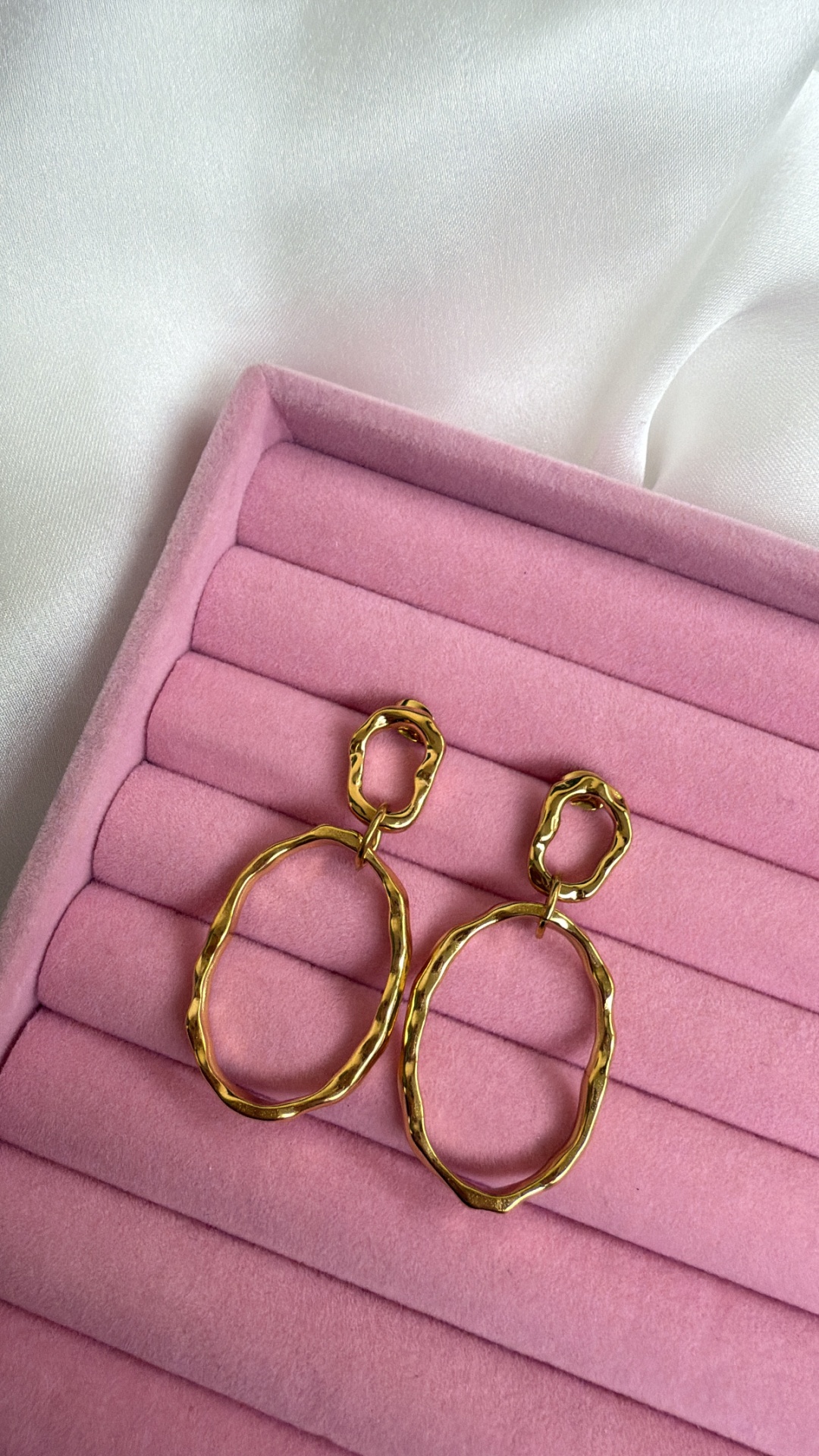 Brincos dourados em forma oval em caixa de veludo rosa