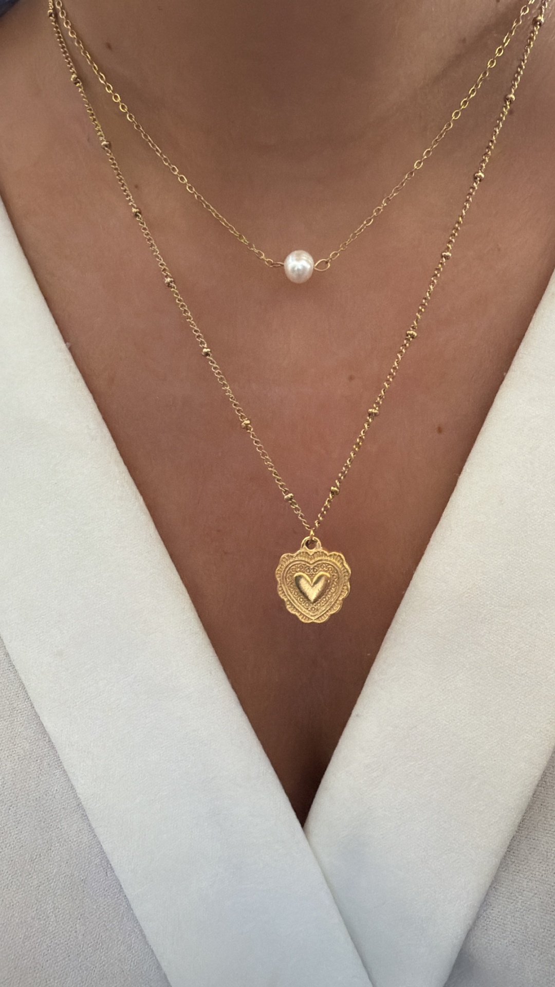 Colares dourados com pérola e pendente de coração no pescoço