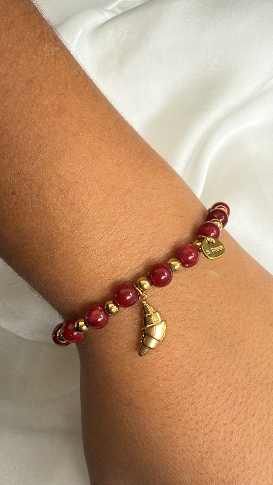 Pulseira vermelha e dourada com pendente em forma de croissant no pulso