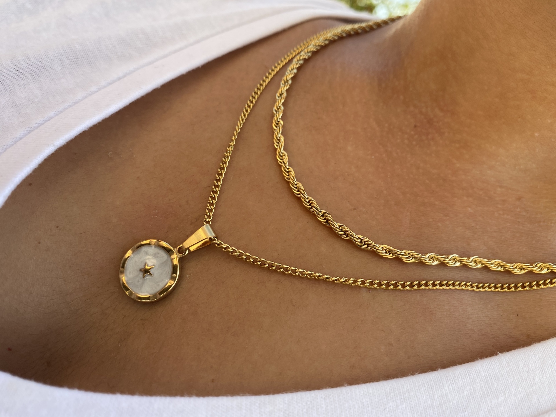 Colar dourado com pendente redondo branco e detalhe de estrela no centro