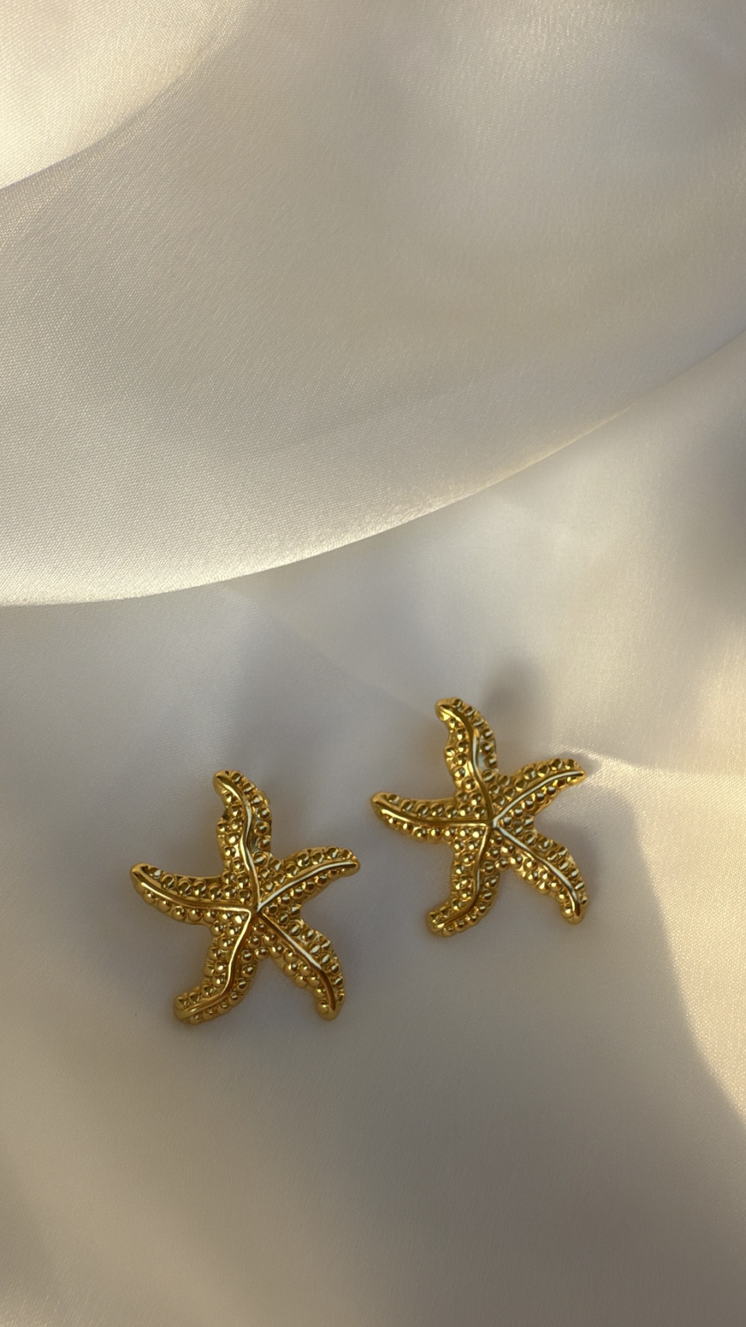 Brincos dourados em forma de estrela-do-mar sobre tecido branco