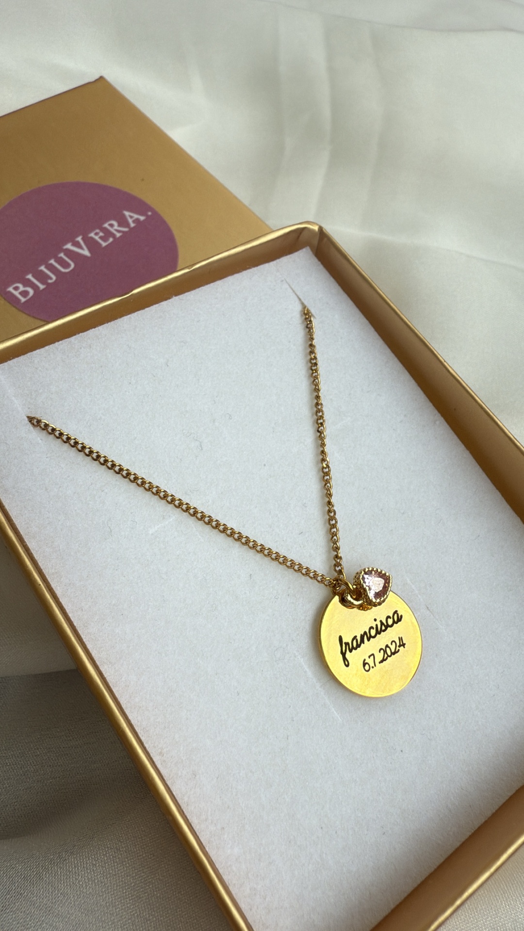 Colar dourado com pendente redondo gravado e pedra rosa em caixa dourada