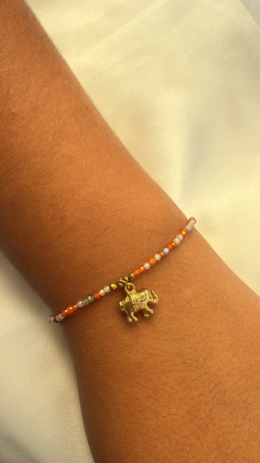 Pulseira de contas coloridas com pendente de elefante dourado no pulso.